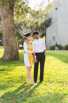 a man and woman in graduation gowns standing under a tree