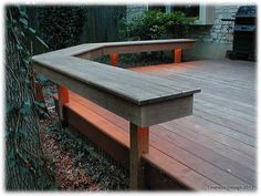 a wooden bench sitting on top of a wooden deck next to a tree and bushes