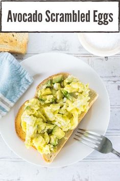 an avocado scrambled egg sandwich on a white plate with a fork next to it