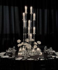 a table with candles and plates on it in the middle of a dark room filled with chairs