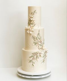 a three tiered wedding cake with white flowers and leaves painted on the bottom layer