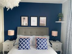 a bedroom with blue walls, white bedding and two framed pictures on the wall