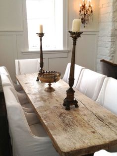 a wooden table with two candles on it in front of a white couch and window