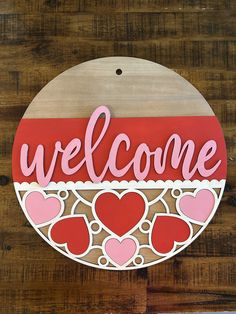 a wooden sign that says welcome with hearts on the front and bottom, hanging on a wall