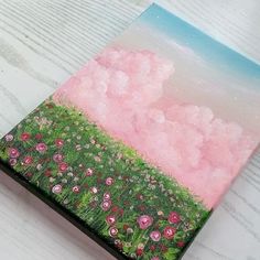 a painting is shown on top of a wooden table with flowers and clouds in the sky