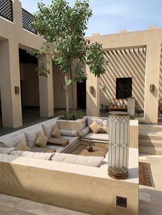 an outdoor living area with couches, tables and potted trees in the background