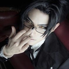 a man with black hair and glasses is holding his hand up to his face while sitting in a chair