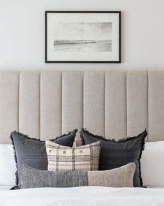 a bed with two pillows on top of it next to a framed painting above the headboard