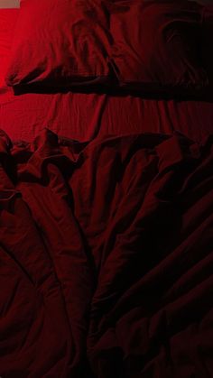 an unmade bed with red sheets and pillows