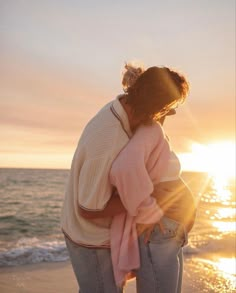 a woman standing on top of a sandy beach next to the ocean at sun set