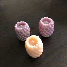 three small pink flowers sitting on top of a wooden table next to an orange candle