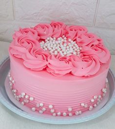 a pink cake decorated with flowers and pearls on a plate in front of a white wall