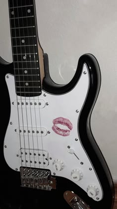 a black and white guitar with lipstick on it's pick - up case sitting next to a wall