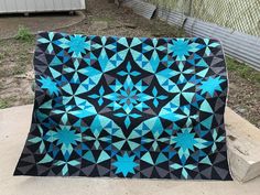 a blue and black quilt sitting on top of a cement slab next to a fence