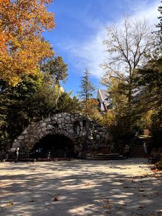 a stone tunnel in the middle of a park with lots of trees and leaves around it