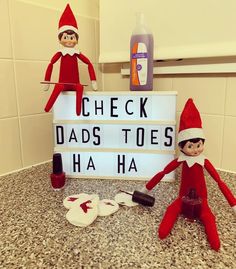 two elfs are sitting next to a sign that says check dad's toes ha ha