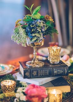 a table topped with books and flowers on top of each other next to candle holders