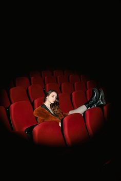 a woman is sitting in the middle of an empty theater seat with her legs crossed