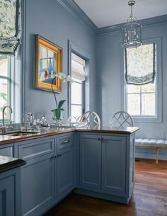 a kitchen with blue painted walls and wooden floors is pictured in this image, there are two chandeliers hanging from the ceiling