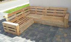 a wooden bench sitting on top of a brick floor next to a white wall and green grass