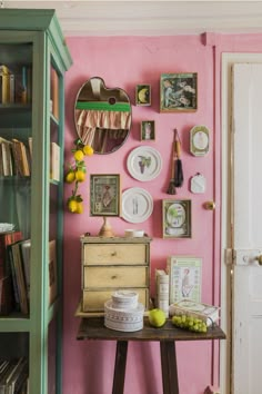 a room with pink walls and pictures on the wall, bookshelf in the background