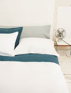 a bed with two pillows and a fan next to it on the floor in front of a white wall