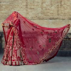 a woman in a red and gold bridal gown is holding her veil over her head