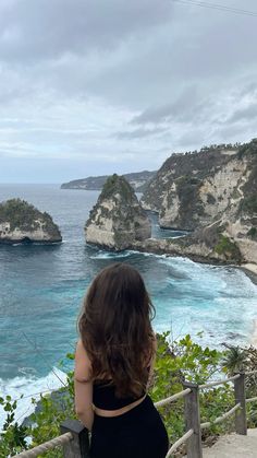 a woman standing on top of a wooden railing next to the ocean with cliffs in the background