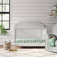 a baby crib in the corner of a room with a chair and potted plant