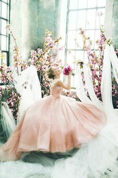 a woman in a pink dress is sitting on the ground with flowers and veils around her