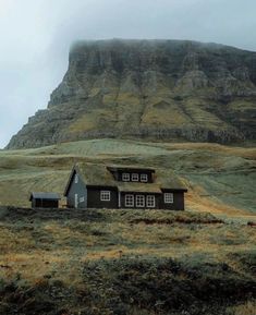 a house in the middle of a field with a mountain behind it