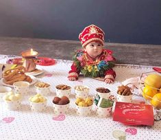 a baby is sitting at a table with many cups and bowls of food on it