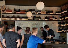 a group of people standing in front of a counter filled with bottles and wine glasses