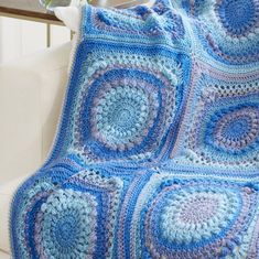 a blue crocheted blanket sitting on top of a white couch next to a plant