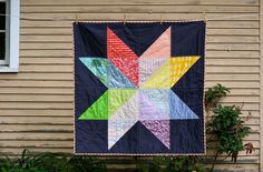 a quilt hanging from a clothes line on the side of a house