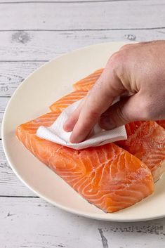 a person is cleaning salmon on a plate with a cloth in their hand and another piece of fish sitting on top of the plate