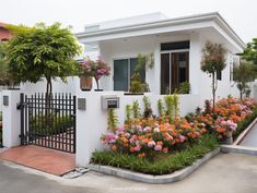 a white house with colorful flowers in the front yard and gated driveway area on both sides