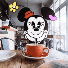 a mickey mouse cutout sitting on top of a wooden table next to a cup of coffee