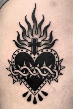 a cross and heart tattoo on the side of a woman's thigh, with flames coming out of it