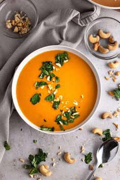 a bowl of carrot soup with cashews and parsley on the side next to it