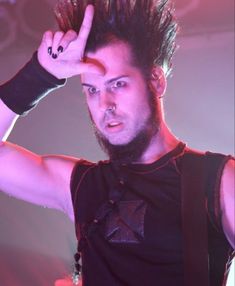 a man with spiked hair holding his hand up in the air while standing on stage