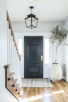 an entryway with a black door, white stairs and a plant in a vase