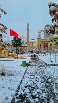 two people walking down a snowy path in front of a tall building with a red flag