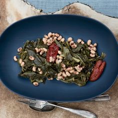 a blue plate topped with spinach and beans next to a silver fork on top of a table