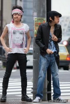 two young men standing next to each other on a street corner near a crosswalk