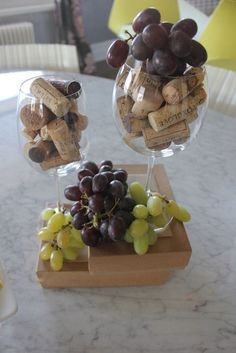 two wine goblets filled with grapes and corks on top of a table