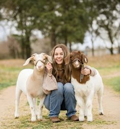 a woman kneeling down next to three goats