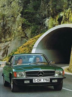 a green car driving past a tunnel on the side of a road with two people in it