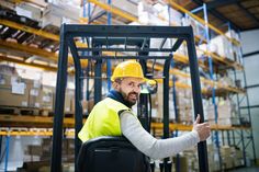 a man in a yellow safety vest is driving a forklift and giving the thumbs up