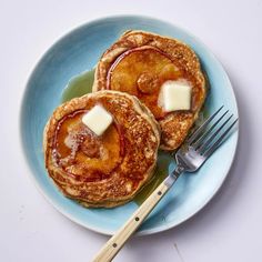 two pancakes with butter and syrup on a blue plate next to a knife and fork